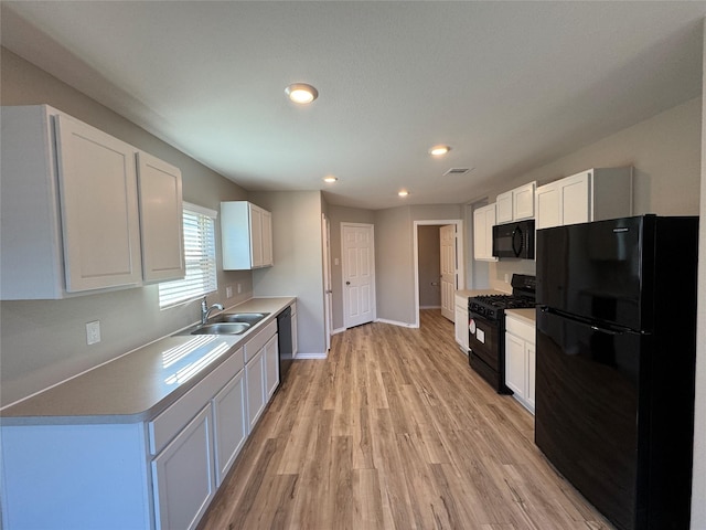 kitchen with visible vents, light wood-style floors, black appliances, white cabinetry, and a sink