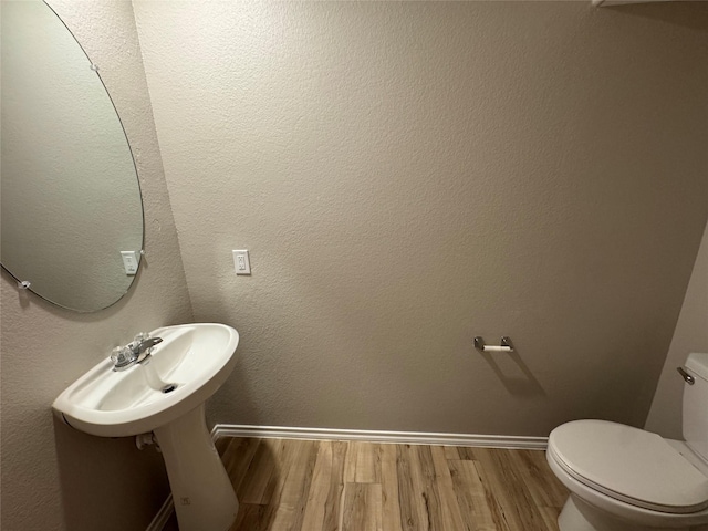 half bath with a textured wall, wood finished floors, toilet, and baseboards