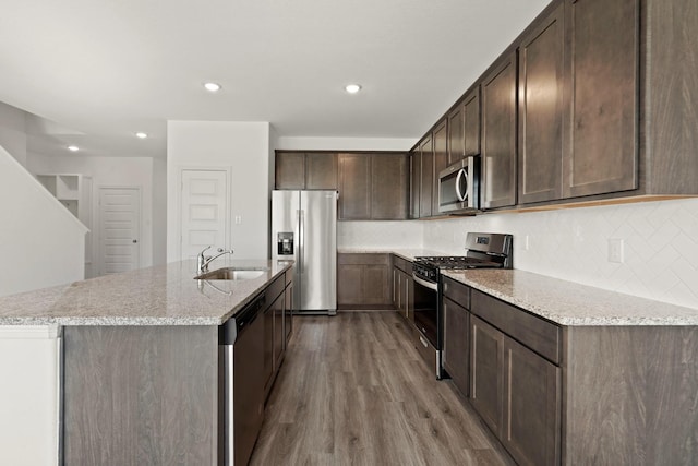 kitchen with sink, stainless steel appliances, dark brown cabinetry, light stone counters, and wood-type flooring