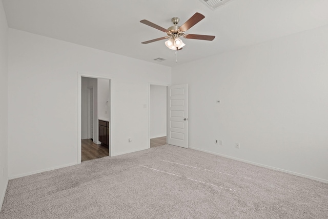 unfurnished bedroom with ceiling fan, ensuite bathroom, and dark colored carpet