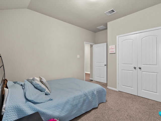 bedroom with vaulted ceiling, carpet floors, a closet, and a textured ceiling