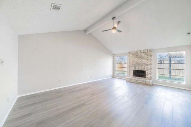 unfurnished living room featuring a fireplace, vaulted ceiling with beams, ceiling fan, light hardwood / wood-style floors, and a textured ceiling