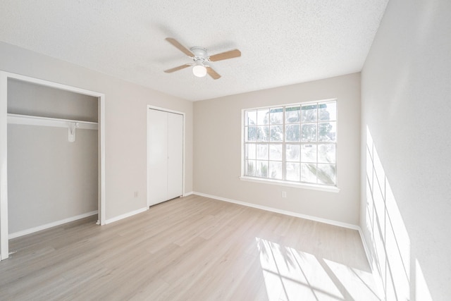 unfurnished bedroom featuring multiple closets, ceiling fan, light hardwood / wood-style flooring, and a textured ceiling