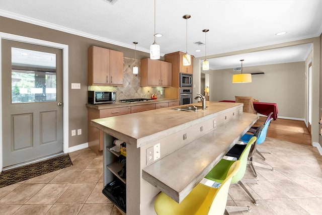 kitchen featuring appliances with stainless steel finishes, tasteful backsplash, hanging light fixtures, ornamental molding, and a center island with sink