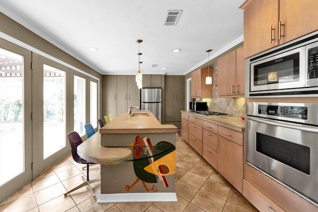 kitchen featuring decorative light fixtures, tasteful backsplash, sink, stainless steel appliances, and a center island with sink