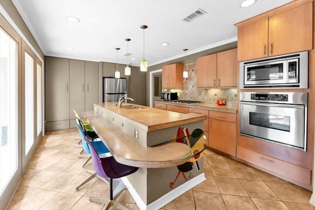 kitchen featuring sink, light tile patterned floors, appliances with stainless steel finishes, hanging light fixtures, and a center island with sink