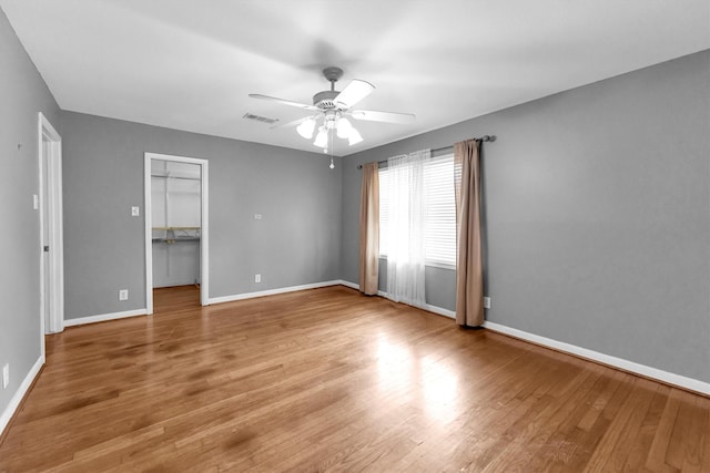 unfurnished bedroom with a spacious closet, hardwood / wood-style floors, ceiling fan, and a closet