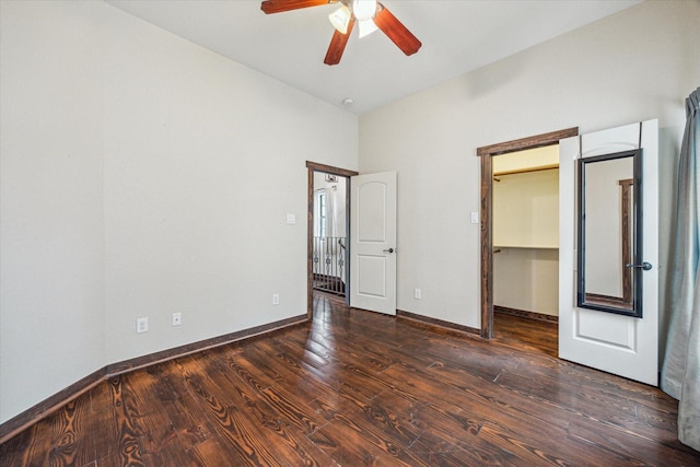 unfurnished bedroom with ceiling fan, a walk in closet, and dark hardwood / wood-style flooring