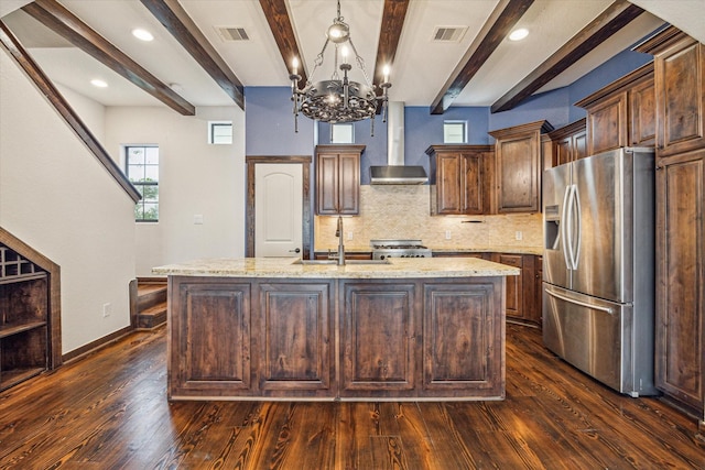 kitchen with wall chimney exhaust hood, sink, stainless steel fridge with ice dispenser, hanging light fixtures, and an island with sink