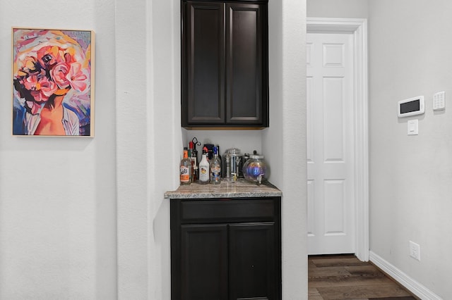 bar with dark hardwood / wood-style floors and light stone counters