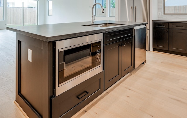 kitchen featuring built in microwave, sink, light hardwood / wood-style flooring, and an island with sink