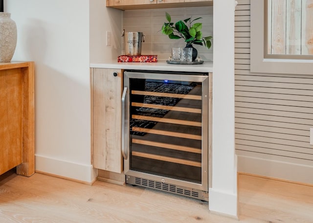 bar with beverage cooler, light wood-type flooring, and decorative backsplash