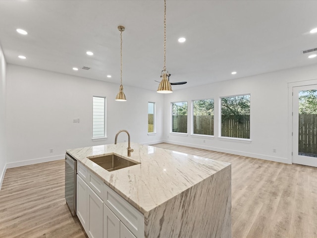 kitchen featuring light stone counters, sink, a center island with sink, and white cabinets