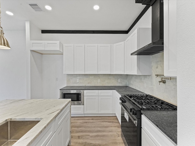 kitchen with wall chimney exhaust hood, white cabinetry, light wood-type flooring, stainless steel microwave, and black gas range