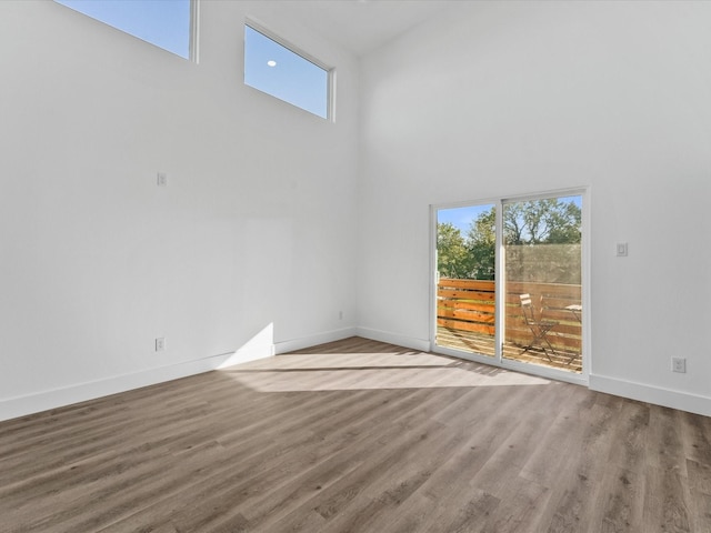 unfurnished room with a towering ceiling, hardwood / wood-style floors, and a wealth of natural light