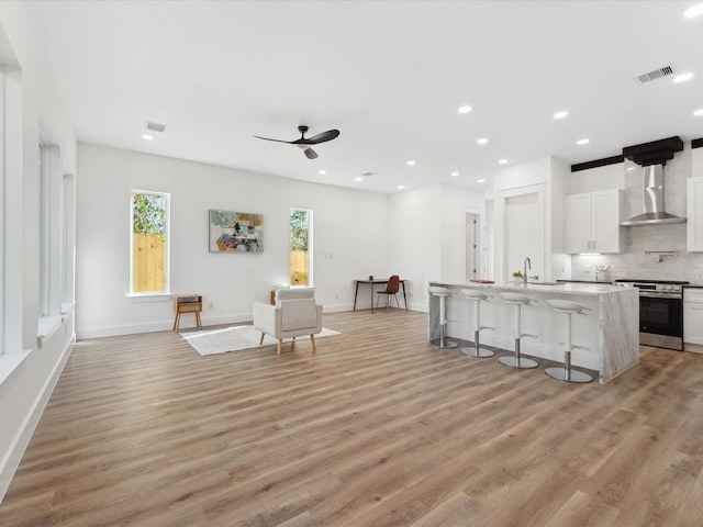 kitchen featuring wall chimney exhaust hood, a breakfast bar area, white cabinetry, a center island with sink, and stainless steel stove