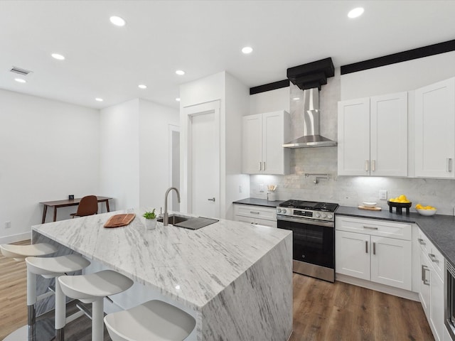 kitchen featuring wall chimney exhaust hood, stainless steel range with gas stovetop, sink, and a center island with sink