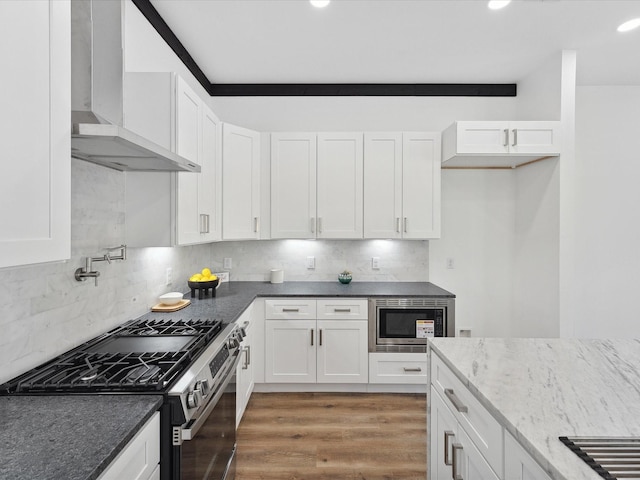 kitchen featuring wall chimney range hood, dark wood-type flooring, stainless steel appliances, tasteful backsplash, and white cabinets