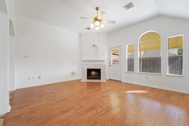 unfurnished living room with ceiling fan, a tiled fireplace, vaulted ceiling, and light hardwood / wood-style flooring