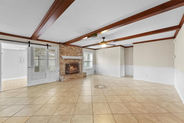 unfurnished living room with ceiling fan, a fireplace, light tile patterned flooring, a barn door, and beamed ceiling