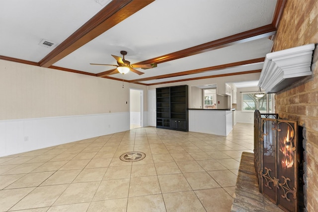 unfurnished living room featuring a fireplace, beamed ceiling, ornamental molding, light tile patterned floors, and ceiling fan