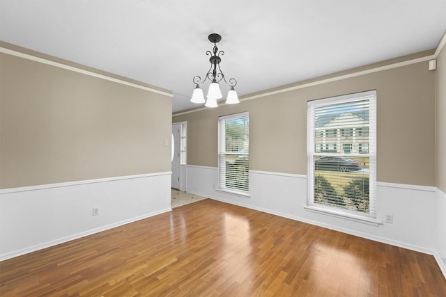 empty room featuring hardwood / wood-style flooring, crown molding, and a chandelier