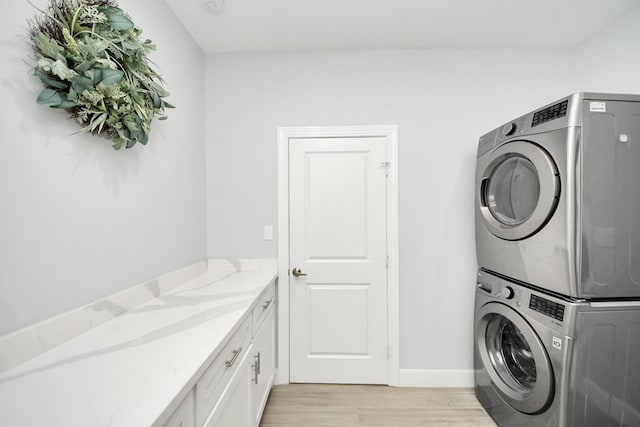 laundry area with stacked washer / dryer, cabinets, and light wood-type flooring