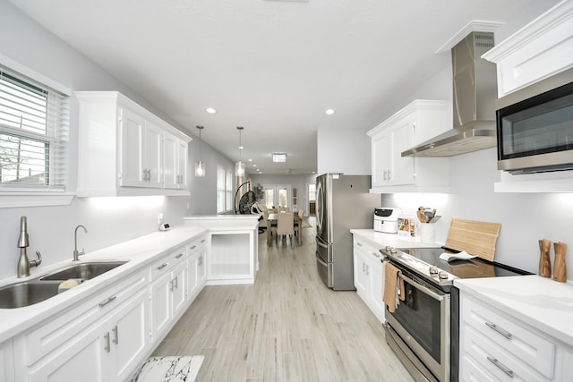 kitchen featuring sink, appliances with stainless steel finishes, pendant lighting, wall chimney range hood, and white cabinets