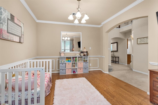 bedroom featuring ornamental molding, a nursery area, hardwood / wood-style floors, and an inviting chandelier