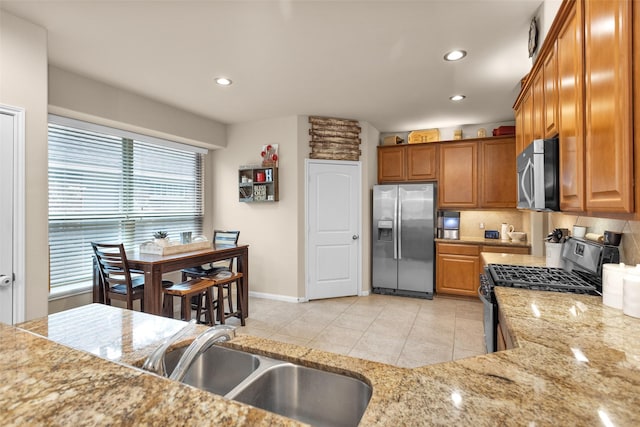 kitchen with appliances with stainless steel finishes, sink, backsplash, light tile patterned floors, and light stone countertops