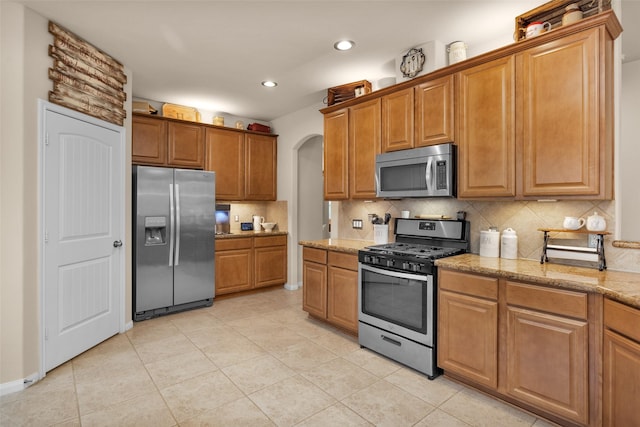 kitchen featuring light stone counters, backsplash, stainless steel appliances, and light tile patterned flooring