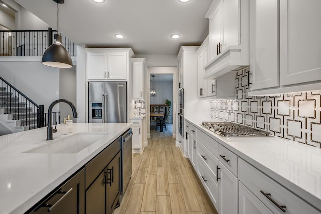 kitchen with pendant lighting, white cabinetry, sink, light stone counters, and stainless steel appliances