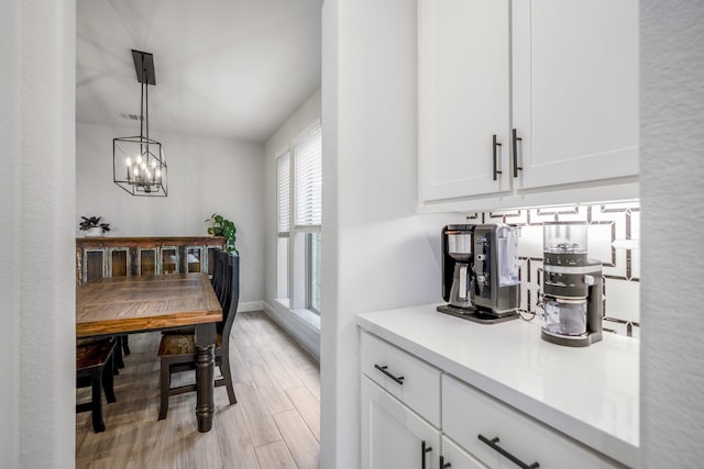 interior space with light hardwood / wood-style floors, hanging light fixtures, and white cabinets