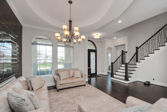 living room featuring a raised ceiling, wood-type flooring, ornamental molding, and a notable chandelier