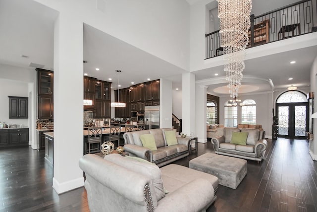 living room featuring ornate columns, a high ceiling, dark wood-type flooring, an inviting chandelier, and french doors