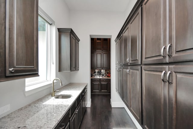 kitchen with sink, dark brown cabinets, light stone countertops, and dark hardwood / wood-style floors