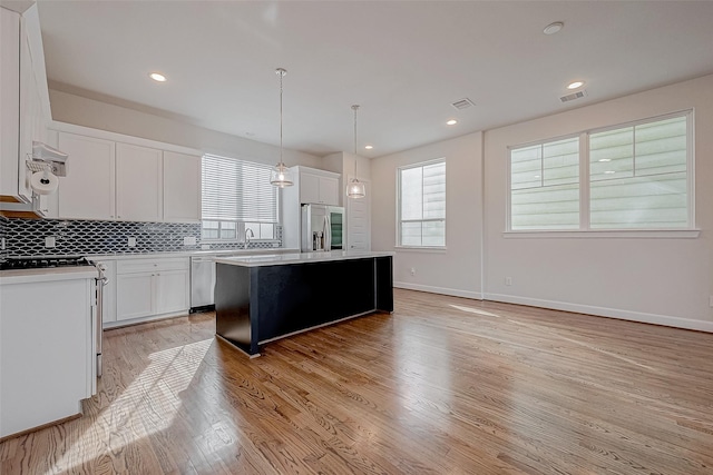 kitchen with appliances with stainless steel finishes, a center island, white cabinets, and decorative light fixtures