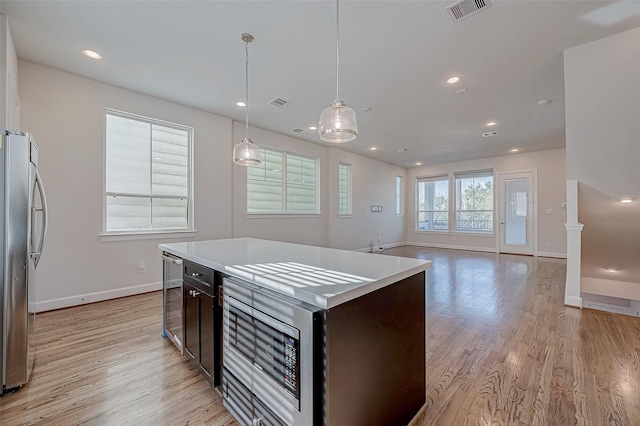 kitchen with stainless steel refrigerator, wine cooler, a kitchen island, decorative light fixtures, and light wood-type flooring