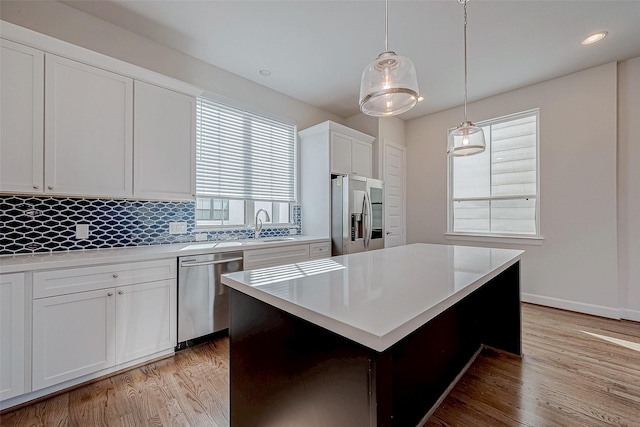 kitchen with a kitchen island, appliances with stainless steel finishes, decorative light fixtures, white cabinets, and light hardwood / wood-style floors