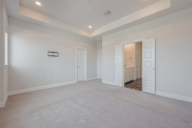 unfurnished bedroom featuring a raised ceiling, dark carpet, and ensuite bath