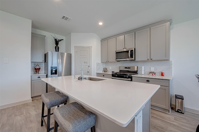 kitchen with sink, a breakfast bar, appliances with stainless steel finishes, gray cabinetry, and an island with sink