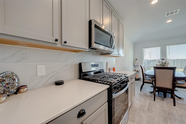 kitchen with backsplash, vaulted ceiling, stainless steel appliances, and light hardwood / wood-style floors