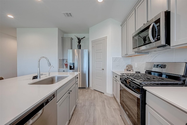 kitchen with tasteful backsplash, appliances with stainless steel finishes, sink, and light hardwood / wood-style floors