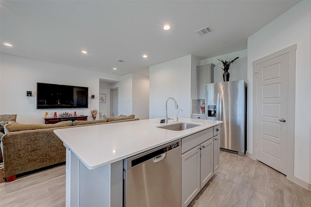 kitchen featuring stainless steel appliances, sink, light hardwood / wood-style floors, and an island with sink