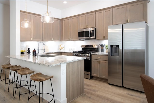 kitchen with pendant lighting, sink, appliances with stainless steel finishes, light stone countertops, and kitchen peninsula