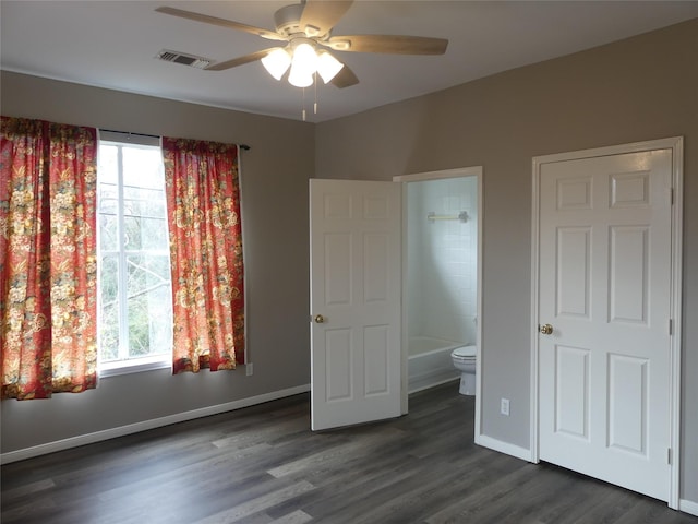 unfurnished bedroom with multiple windows, ensuite bathroom, ceiling fan, and dark hardwood / wood-style flooring