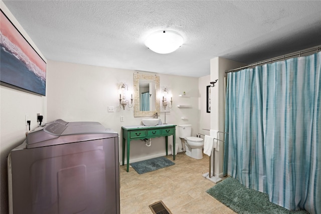 bathroom with curtained shower, sink, washer and clothes dryer, toilet, and a textured ceiling