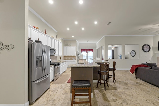 kitchen with light stone countertops, stainless steel appliances, white cabinets, and a center island with sink