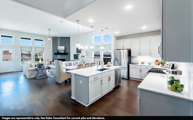 kitchen with sink, hanging light fixtures, a center island with sink, stainless steel appliances, and white cabinets