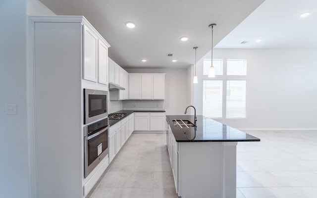 kitchen featuring a sink, white cabinets, hanging light fixtures, appliances with stainless steel finishes, and a center island with sink